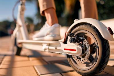 Close-up of a woman's feet on an electric scooter, focusing on the wheel in the foreground.