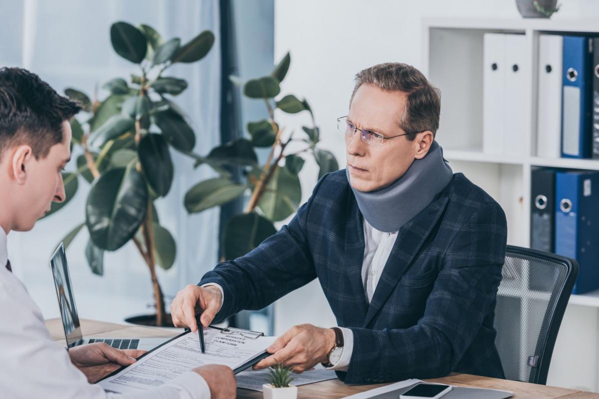 businessman in neck brace sitting at table and pointing at form for workers' compensation